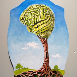 May include: A wooden wall art piece featuring a brain-shaped tree with a blue sky background. The brain is yellow and green, the tree trunk is brown, and the roots are a lighter brown. The background includes green hills and a few white clouds.