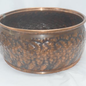 May include: A hammered copper planter with a textured surface. The planter is round and has a wide opening.