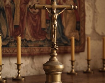 May include: A brass crucifix standing on a circular base with three small feet. The cross features a figure of Jesus, the letters INRI at the top, and a skull and crossbones symbol at the base of the vertical beam. The metal has a muted finish.