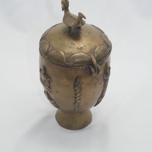 Peut inclure: Un récipient en laiton avec un couvercle orné d'un bouton en forme d'oiseau. Le récipient a un corps rond avec des détails décoratifs et un pied court et rond.