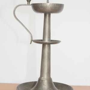 May include: A silver metal oil lamp with a handle and a round base. The lamp has a single wick and a small, round knob on the top.