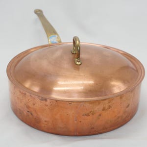 May include: A copper saucepan with a brass handle and lid. The saucepan has a hammered finish and is showing signs of wear.