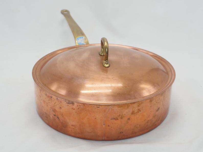 May include: A copper saucepan with a brass handle and lid. The saucepan has a hammered finish and is showing signs of wear.