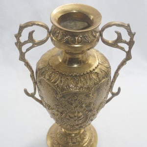 May include: A gold metal vase with ornate details and two handles. The vase has a round body and a flared base.