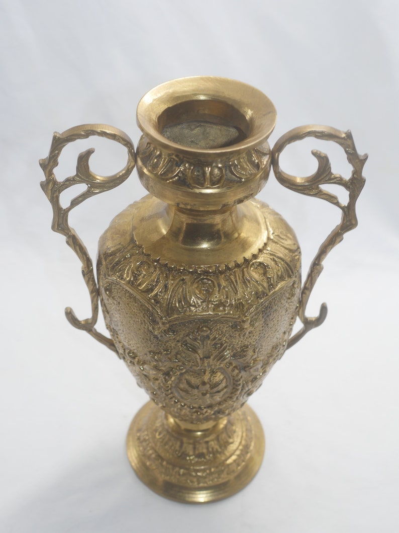 May include: A gold metal vase with ornate details and two handles. The vase has a round body and a flared base.