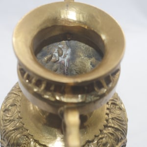 May include: A gold metal incense burner with intricate details and a wide opening at the top. The burner has a worn, aged look, with some discoloration on the inside.