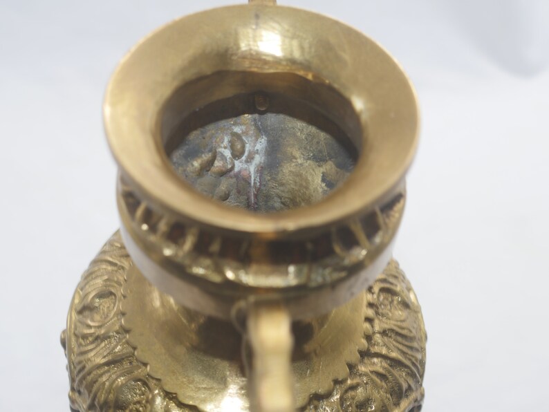 May include: A gold metal incense burner with intricate details and a wide opening at the top. The burner has a worn, aged look, with some discoloration on the inside.
