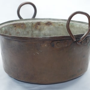 May include: A large, antique copper pot with two sturdy iron handles. The pot has a worn, aged patina and shows signs of use.
