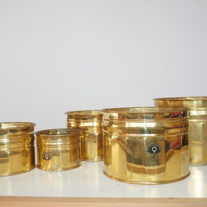 Peut inclure: Ensemble de cinq pots de fleurs en métal doré de tailles différentes. Chaque pot a un design cannelé et un petit logo circulaire avec le texte "Danish Design" sur le côté.