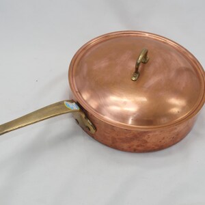 May include: A copper saucepan with a brass handle and a lid. The saucepan has a hammered finish.