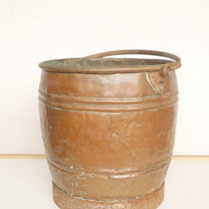 May include: A copper bucket with a metal handle and a rusty base. The bucket has a hammered texture and a greenish patina.