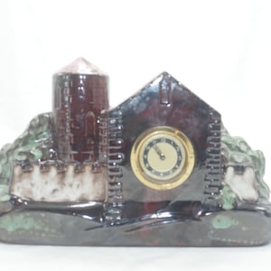 May include: A ceramic clock shaped like a castle with a brown, green and white glaze. The clock face is round and has black hands.