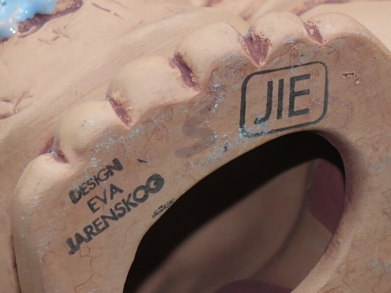 Pu&ograve; includere: Primo piano della parte inferiore di una statuetta in ceramica color terracotta. La statuetta ha un foro sul fondo e il testo "DESIGN EVA JARENSKOO" e "JIE" sono stampati sul fondo.