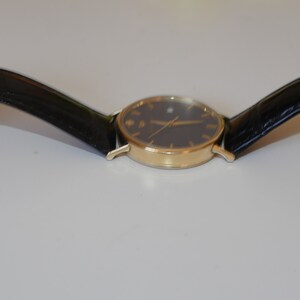May include: A gold-tone wristwatch with a black face and black leather band.