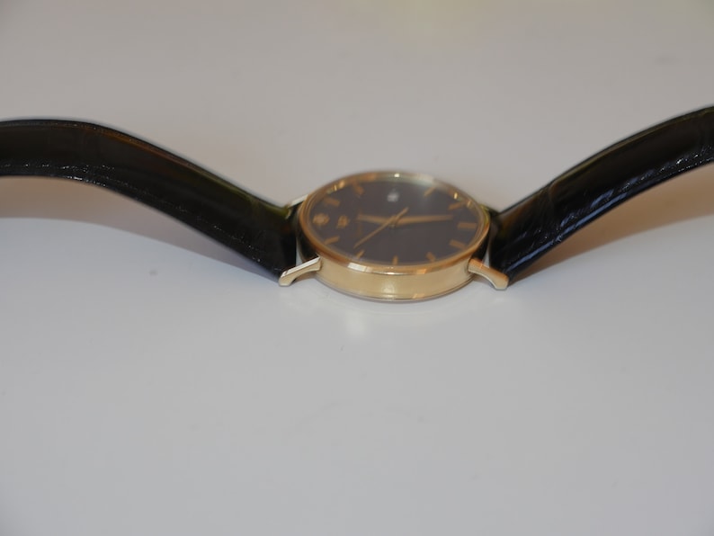 May include: A gold-tone wristwatch with a black face and black leather band.