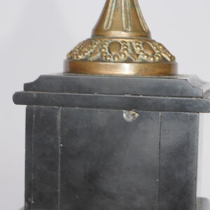 May include: A black marble base with a gold-toned metal top. The top has a decorative design with a pointed finial.