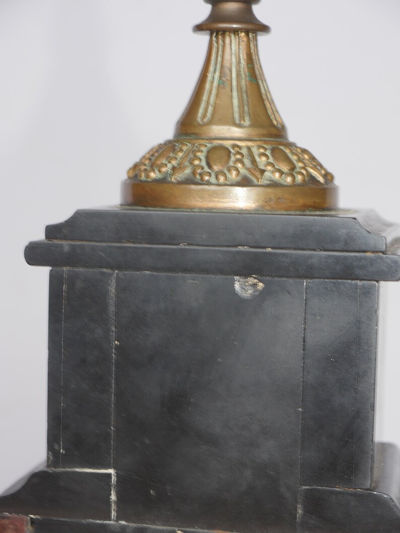 May include: A black marble base with a gold-toned metal top. The top has a decorative design with a pointed finial.