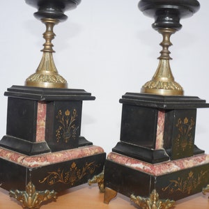 May include: A pair of black and gold candle holders with marble bases. The bases are decorated with gold floral designs.