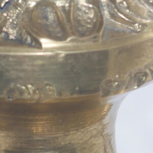 May include: Close-up of the bottom of a brass candlestick with an ornate design. The bottom of the candlestick has a small inscription that reads "Made in Italy".