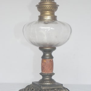 May include: An antique oil lamp with a clear glass globe, a brass burner, and a wooden base with an ornate metal stand.