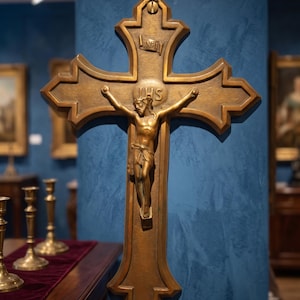 May include: A bronze-toned wall crucifix featuring a central figure of Jesus on the cross. The cross has an ornate, multi-pointed shape with the letters IHS inscribed above the figure and an INRI scroll banner positioned at the top section.