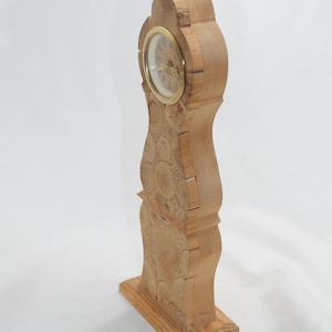 Könnte beinhalten: Eine Holzuhr mit einem runden Zifferblatt und einem einzigartigen Design. Die Uhr ist aus Holz gefertigt und hat eine natürliche Oberfläche. Die Uhr steht auf einer weißen Oberfläche.