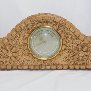 Könnte beinhalten: Eine Holzuhr mit goldenem Zifferblatt und römischen Ziffern. Die Uhr ist aus kleinen Holzstücken gefertigt, die in einem Mosaikmuster angeordnet sind. Die Uhr ist halbkreisförmig und hat ein dekoratives Design am Rand.