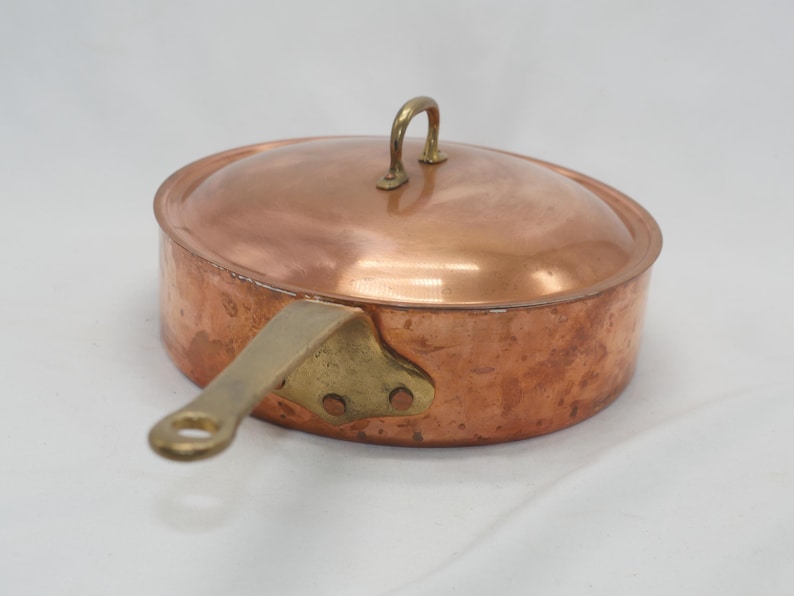 May include: A copper saucepan with a brass handle and lid. The saucepan has a hammered finish and is in good condition.