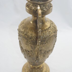 May include: A gold metal vase with an ornate design. The vase has a wide mouth and a narrow base. It is decorated with intricate floral patterns.