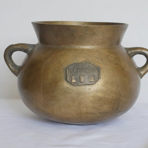 Op de afbeelding: Een grote, ronde, messing pot met twee handvatten. De pot heeft een verhoogde, achthoekige stempel aan de zijkant met de tekst "W. BARBER & CO."
