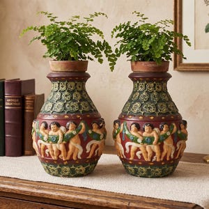 May include: A pair of matching ceramic vases featuring a relief frieze of cherubs holding a green garland against a deep red background. The upper and lower sections are decorated with a dark green textured pattern, and each holds a small green plant.