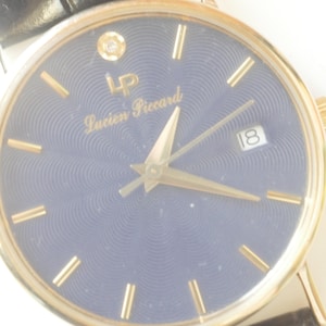 May include: A gold-tone wristwatch with a blue face and gold-tone hands. The watch has a diamond at the 12 o'clock position and the text 'Lucien Piccard' on the face.