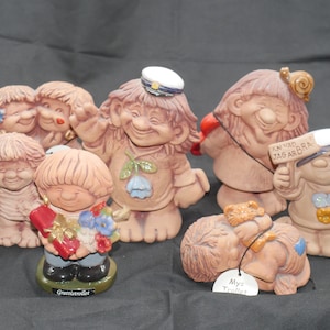 Pu&ograve; includere: Una collezione di sette figurine in ceramica di gnomi, ognuna con dettagli ed espressioni uniche. Alcuni gnomi indossano cappelli, tengono cuori e portano cartelli con testo svedese. Gli gnomi sono dipinti in varie tonalit&agrave; di marrone, rosso, blu e bianco.