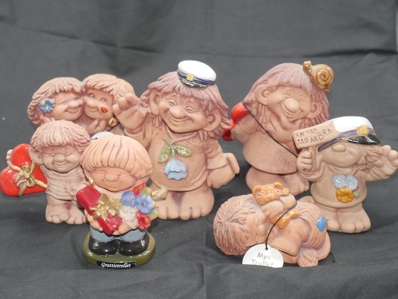 Pu&ograve; includere: Una collezione di sette figurine in ceramica di gnomi, ognuna con dettagli ed espressioni uniche. Alcuni gnomi indossano cappelli, tengono cuori e portano cartelli con testo svedese. Gli gnomi sono dipinti in varie tonalit&agrave; di marrone, rosso, blu e bianco.