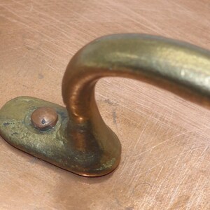 May include: Close-up of a copper pot with a brass handle. The handle is curved and has a small, round knob on the top.
