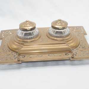 May include: A brass inkwell set with two glass inkwells with lids. The inkwell set has an ornate, filigree design.