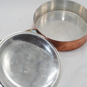May include: A copper pot with a silver lid. The pot has a hammered finish and the lid has a smooth surface.