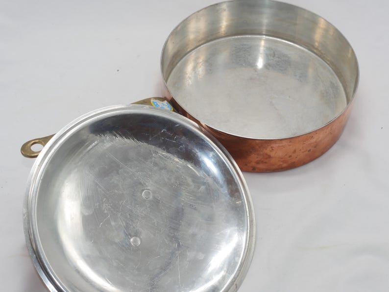 May include: A copper pot with a silver lid. The pot has a hammered finish and the lid has a smooth surface.