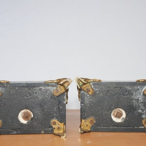 May include: Two black bookends with gold accents and a white marble base. The bookends are shaped like a pair of hands holding a book. The bookends have the numbers 1773 and 1773 inscribed on them.