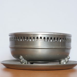 May include: A silver serving bowl with a decorative rim and three feet. The bowl is sitting on a matching silver plate.