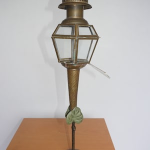 Könnte beinhalten: Eine Messinglampe mit einem Glasschirm und einem dekorativen Sockel. Die Lampe hat ein grünes Blattdesign auf dem Sockel und einen Knauf oben.