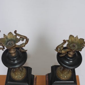 May include: A pair of black and gold candle holders with ornate details. The candle holders are made of metal and have a square base.
