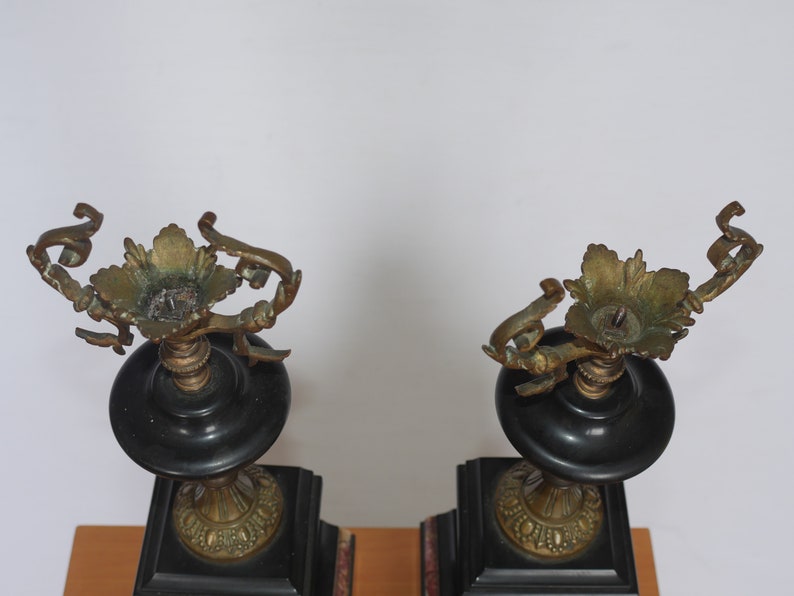May include: A pair of black and gold candle holders with ornate details. The candle holders are made of metal and have a square base.