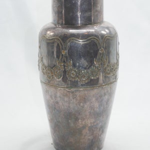 May include: A silver vase with an ornate design of flowers and leaves around the middle. The vase has a slightly rounded body and a narrow opening.