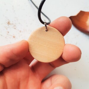 May include: A round wooden pendant with a hole in the centre, attached to a black cord.