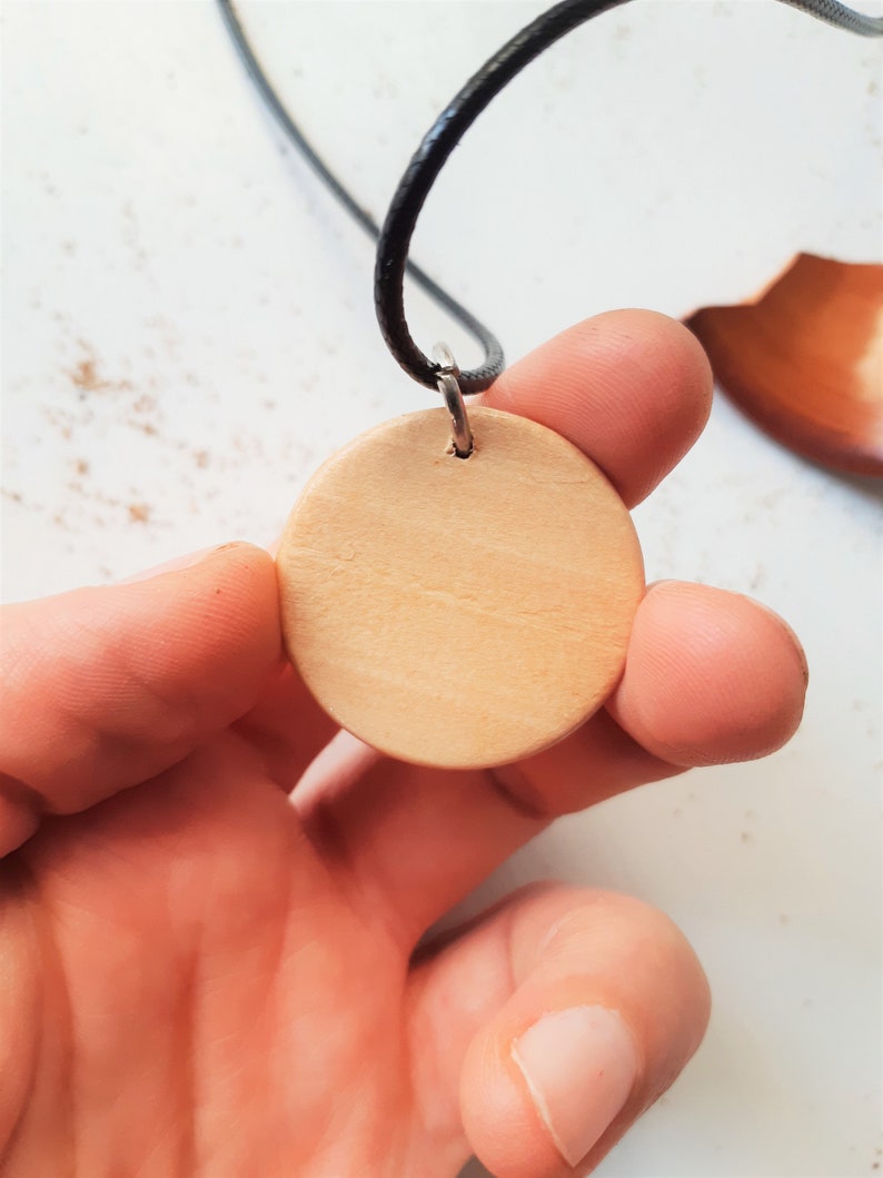 May include: A round wooden pendant with a hole in the centre, attached to a black cord.