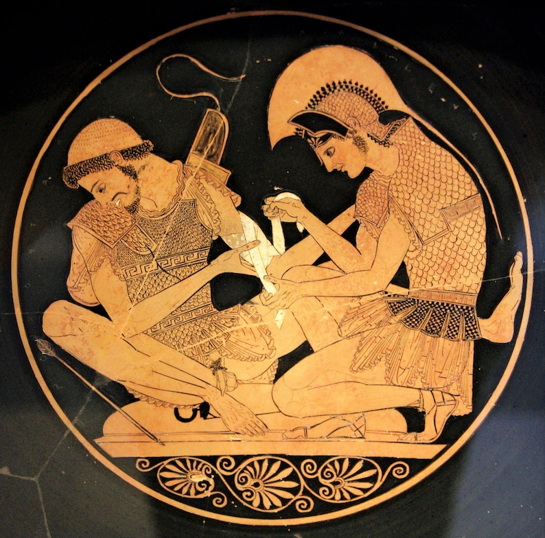 May include: A black and red Greek vase painting depicting two figures. One figure is kneeling and bandaging the leg of the other figure. Both figures are wearing armour and helmets. The background is black with a red border.