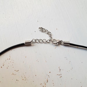May include: Close-up of a black cord necklace with a silver chain extender and lobster clasp.