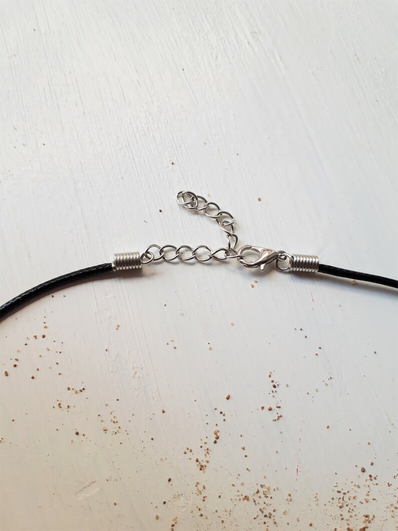 May include: Close-up of a black cord necklace with a silver chain extender and lobster clasp.
