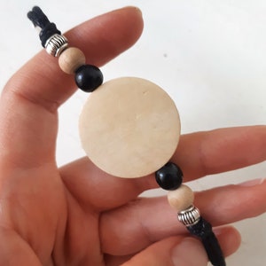Puede incluir: Un brazalete de cord&oacute;n negro con cuentas de madera y plata y un gran dije redondo de madera.